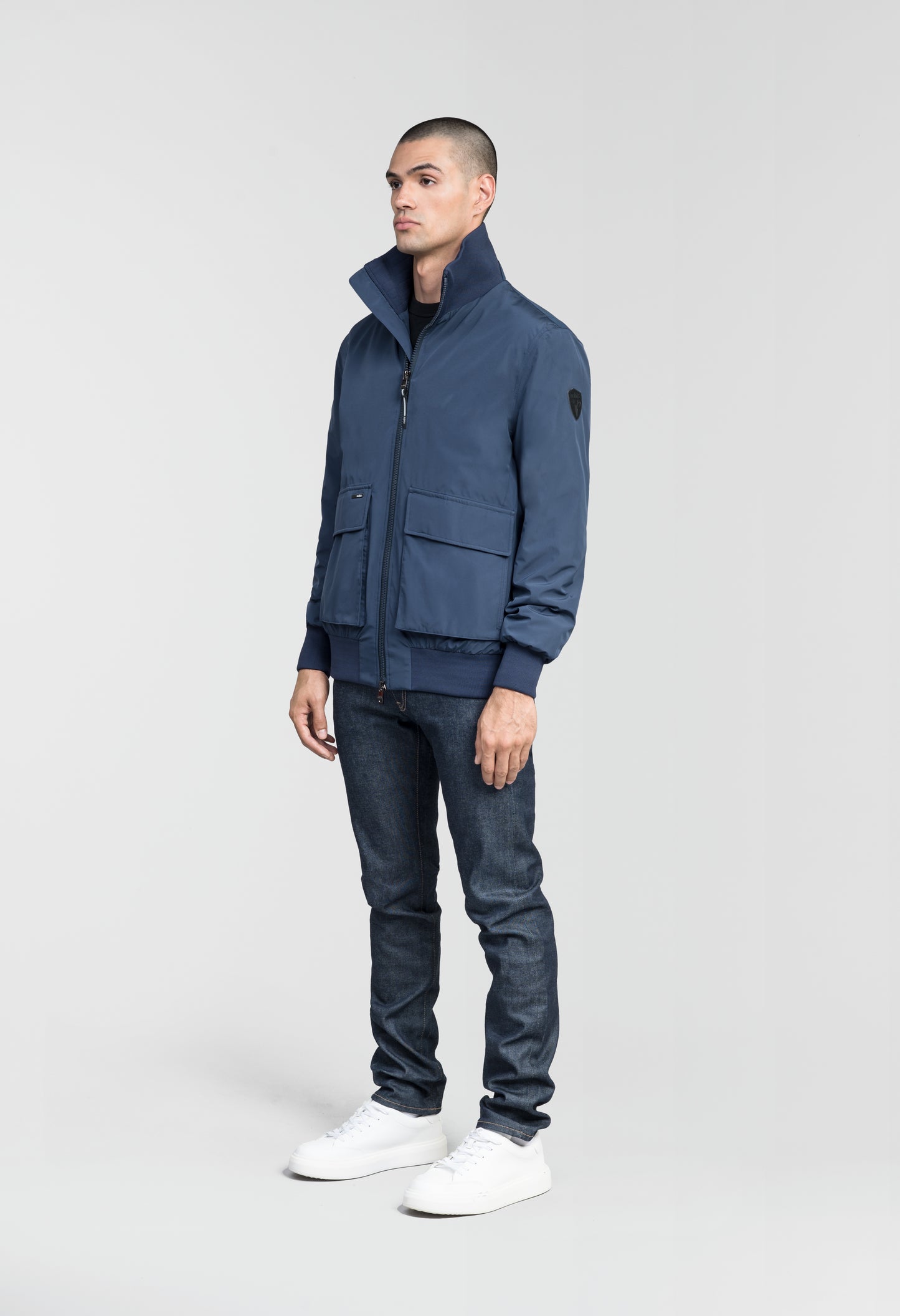 Flint Men's Tailored Rib Collar Jacket in hip length, premium 3-ply Micro Denier fabrication, premium 4-way stretch, water resistant Primaloft Gold Insulation Active +, flap pockets with magnetic closure at waist, side entry pockets at waist, ribbed sleeve cuffs, two-way branded zipper at centre front, box pleat detailing at centre back, large interior zipper pocket, and interior button pocket at left chest, in Marine