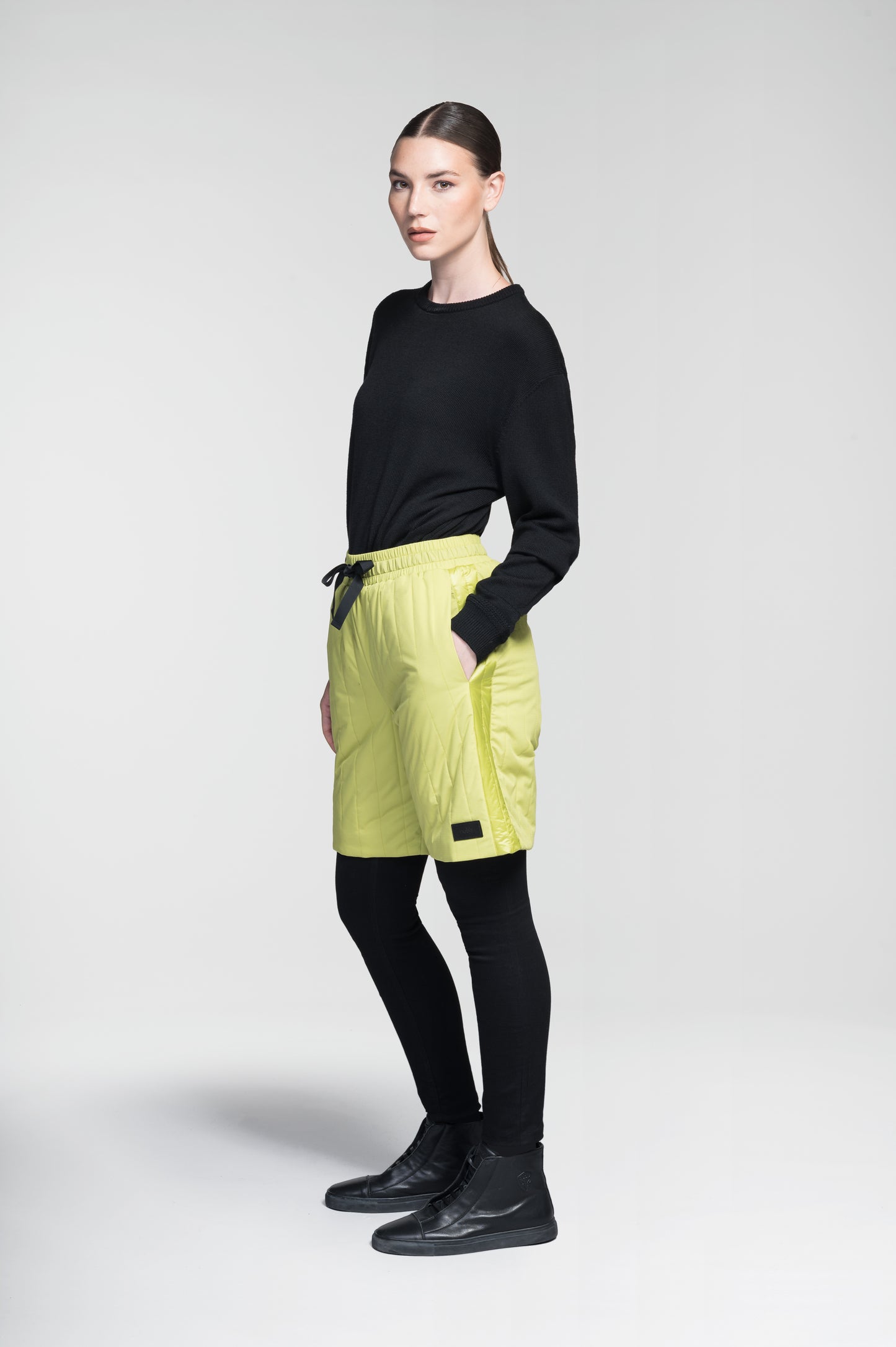 Kit Women's Quilted Shorts in knee length, premium stretch ripstop and contrast cire technical nylon taffeta fabrication, premium 4-way stretch, water resistant Primaloft Gold Insulation Active+, elasticized waistband with grosgrain ribbon drawstrings, hidden side seam toggles for rouching detail, snap closure side seam pockets at hips, and single welt snap button pockets at back, in Black