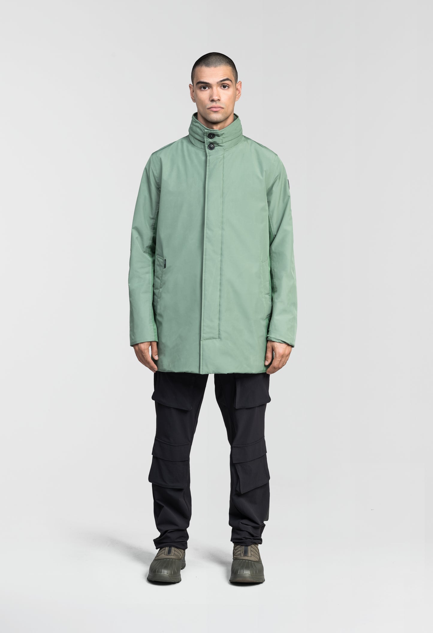 Pike Men's Tailored Mac Coat in thigh length, premium 3-ply Micro Denier fabrication at body and cire technical nylon taffeta fabrication at hood, premium 4-way stretch, water resistant Primaloft Gold Insulation Active+, hidden 2-way zipper with snap closure wind flap, single welt pockets with magnetic closure at waist, hidden snap placket at cuffs, pit zippers for ventilation, interior zipper pocket at right chest, and interior button pocket at left chest, in Comfrey