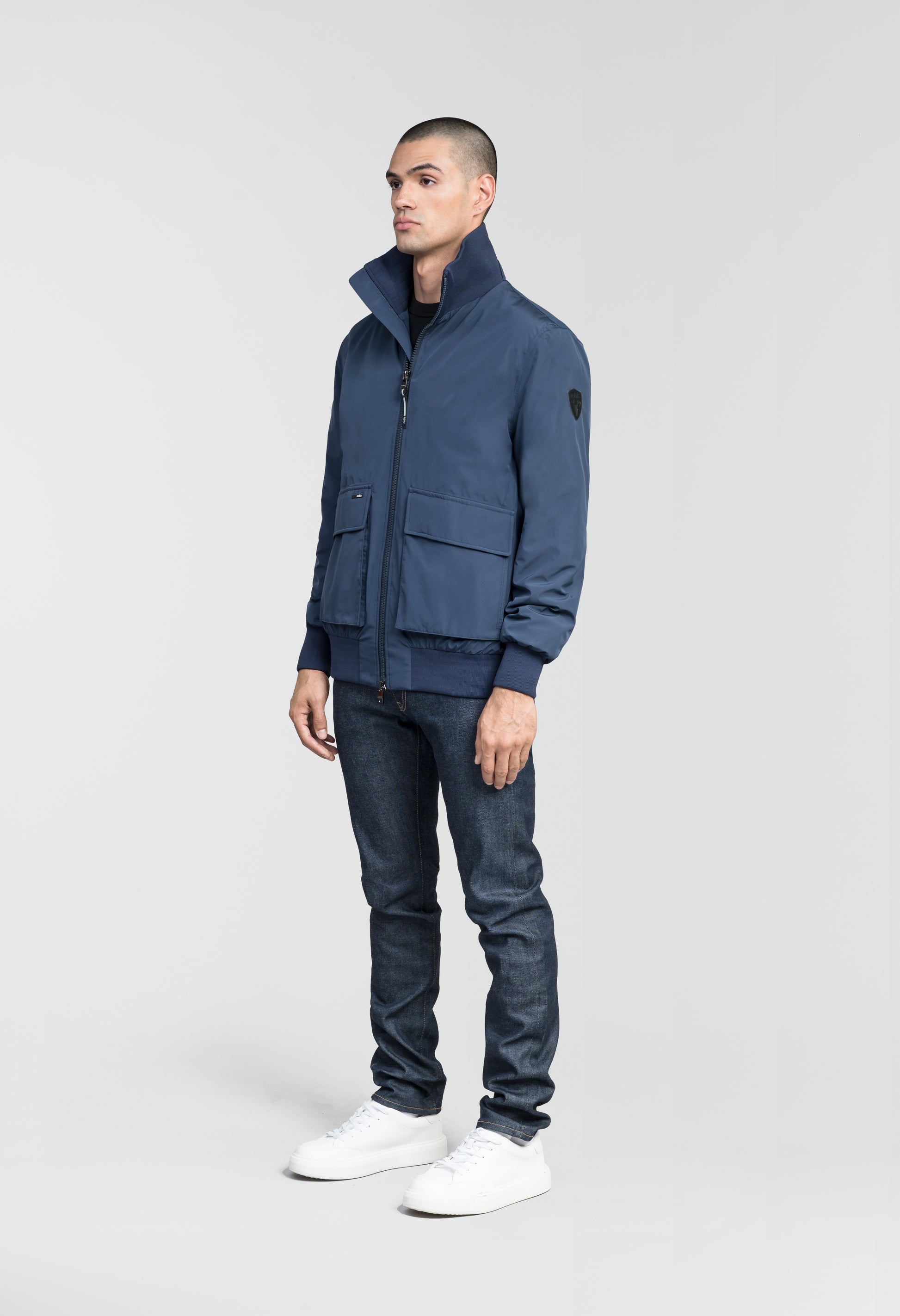 Flint Men's Tailored Rib Collar Jacket in hip length, premium 3-ply Micro Denier fabrication, premium 4-way stretch, water resistant Primaloft Gold Insulation Active +, flap pockets with magnetic closure at waist, side entry pockets at waist, ribbed sleeve cuffs, two-way branded zipper at centre front, box pleat detailing at centre back, large interior zipper pocket, and interior button pocket at left chest, in Marine