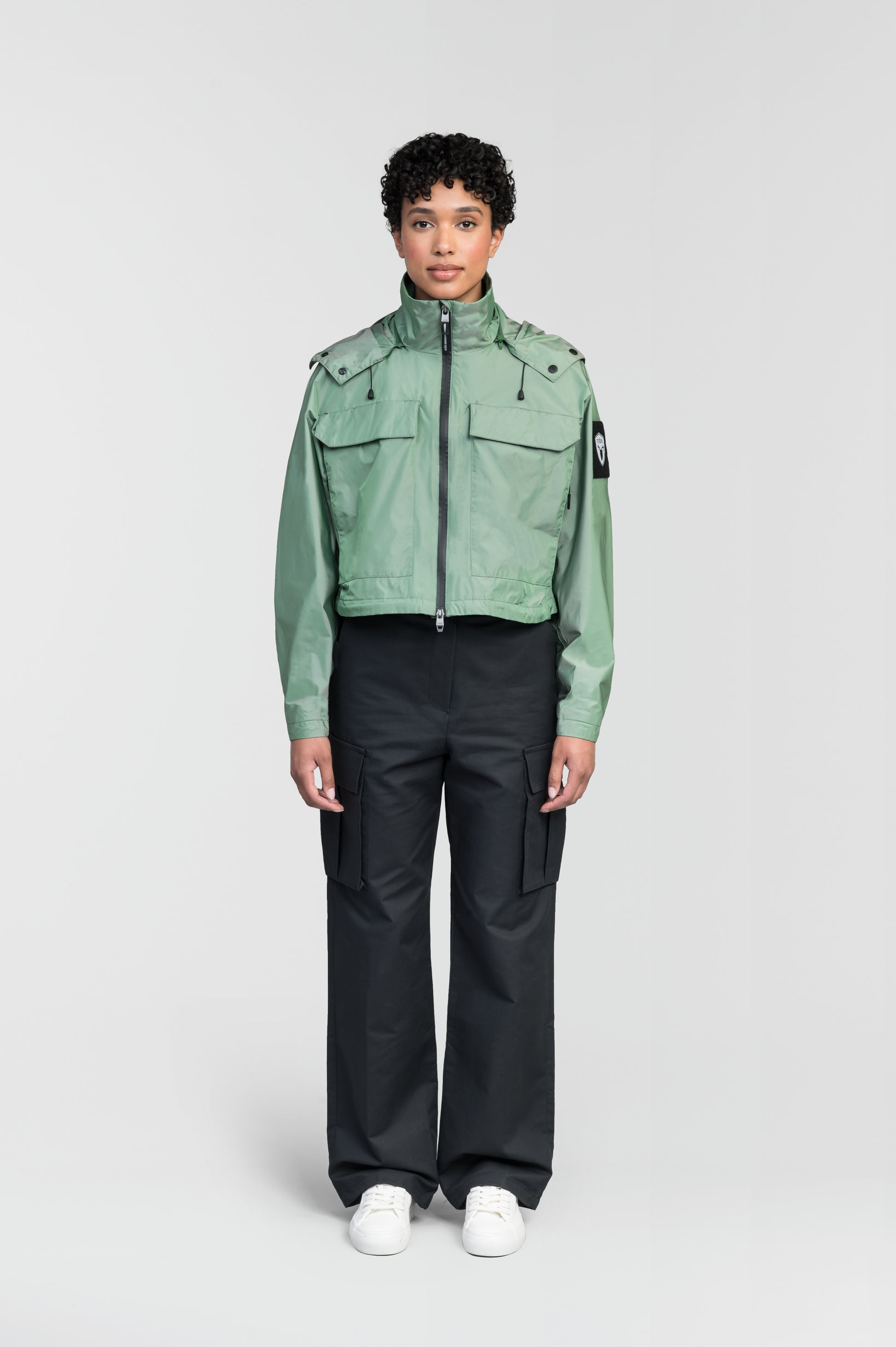Viva Women's Performance Cropped Jacket in waist length, premium iridescent fabrication, removable hood with peak, adjustable hood draw cords and toggle, 2-way branded zipper at centre front, oversized magnetic closure flap pockets at chest with side entry, interior adjustable draw cord at hem, large interior zipper pocket, and adjustable snap cuffs, in Comfrey