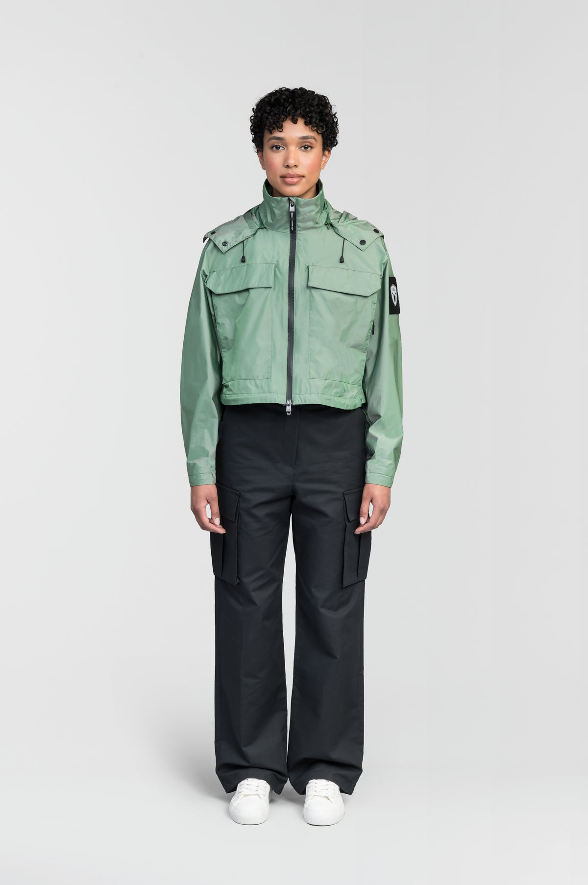 Viva Women's Performance Cropped Jacket in waist length, premium iridescent fabrication, removable hood with peak, adjustable hood draw cords and toggle, 2-way branded zipper at centre front, oversized magnetic closure flap pockets at chest with side entry, interior adjustable draw cord at hem, large interior zipper pocket, and adjustable snap cuffs, in Comfrey